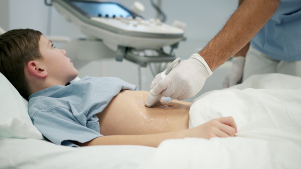 Male doctor using ultrasound probe to check on young boy, abdominal ultrasound.