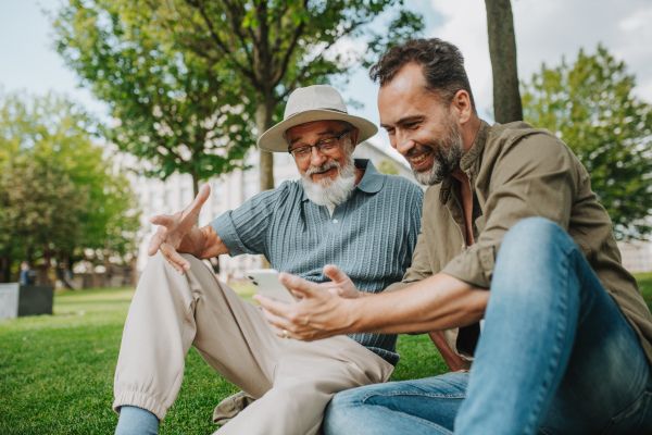 Son showing older father something in smartphone, sharing a joyful moment outdoors