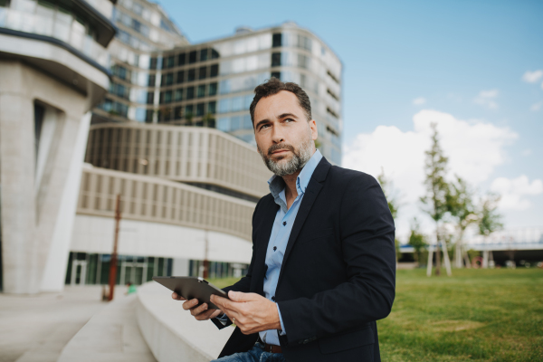 Handsome mature businessman sitting in park with tablet in hand.