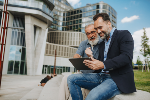 Father and adult son sharing a joyful moment, watching something in tablet. Fathers day concept.