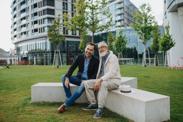 Father and adult son sitting on bench in park, sharing peaceful moment. Fathers day concept.