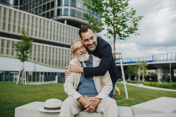 Father and adult son sitting on bench in park, sharing peaceful moment. Fathers day concept.