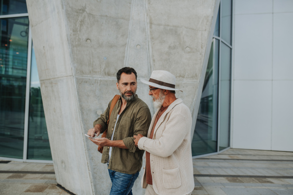 Mature son and father traveling together, looking at map on smartphone.