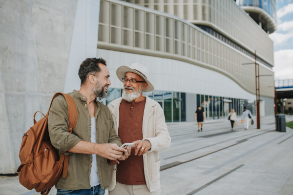 Mature son and father traveling together, looking at map on smartphone.