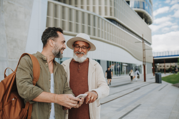 Mature son and father traveling together, looking at map on smartphone.