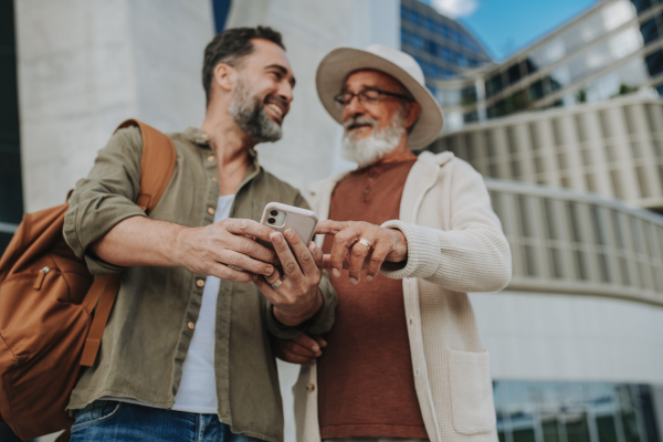 Mature son and father traveling together, looking at map on smartphone.