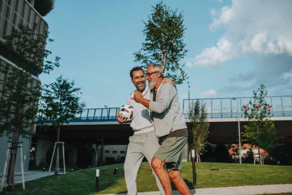 Sporty father and adult son walking home after football match in park. Fathers day concept.