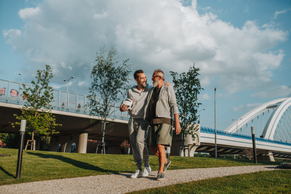 Sporty father and adult son walking home after football match in park. Fathers day concept.