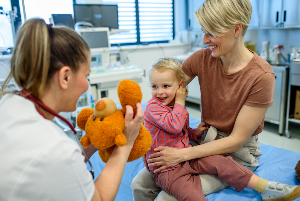 Female pediatrician comforting little boy with teddy bear during checkup