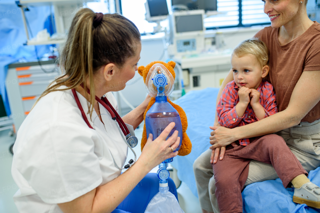 Female pediatrician demonstrates oxygen mask on teddy bear to young patient