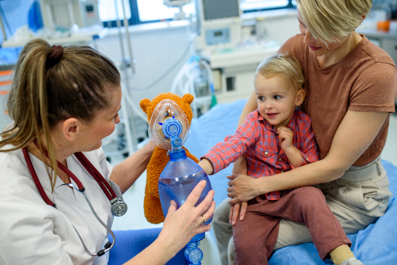 Female pediatrician demonstrates oxygen mask on teddy bear to young patient