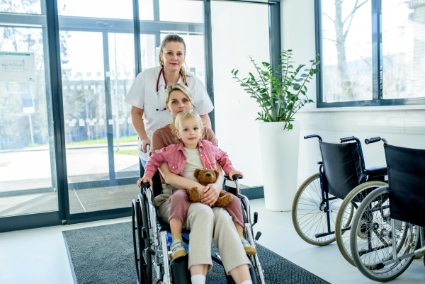 Female doctor or nurse pushing wheelchair with mother and son after treatment