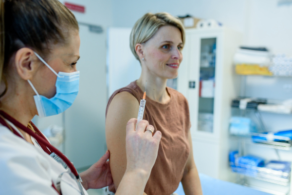 Doctor administering vaccine to woman's arm during routine immunization. Disease prevention.