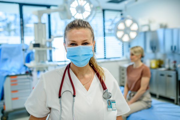 Female doctor in face mask standing in examination room.