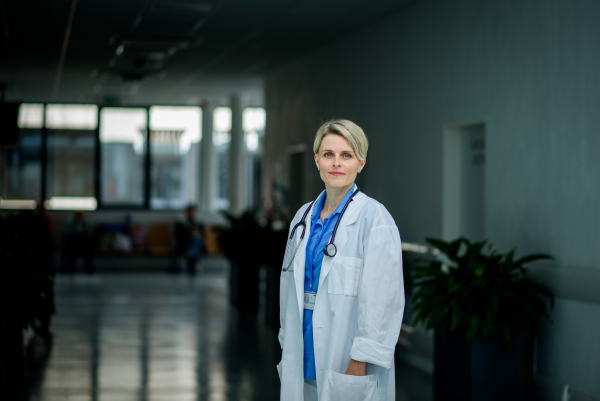 Young female doctor with short hair in hospital corridor, smiling, looking at camera.