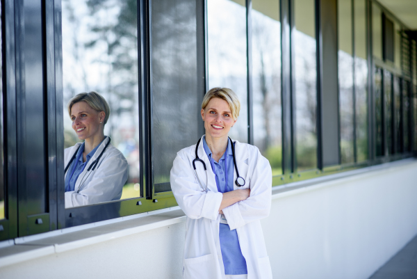 Young female doctor taking a break, standing in front of hospital building.