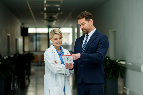 Pharmaceutical sales representative introducing new medication to female doctor, showing her presentation on tablet.
