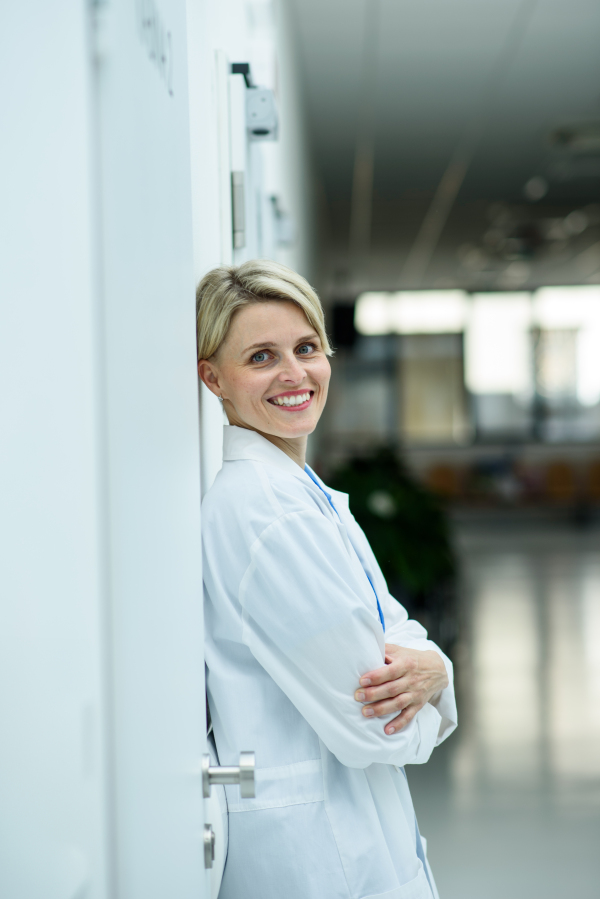Tired female doctor leaning against wall in hospital hallway, side view.