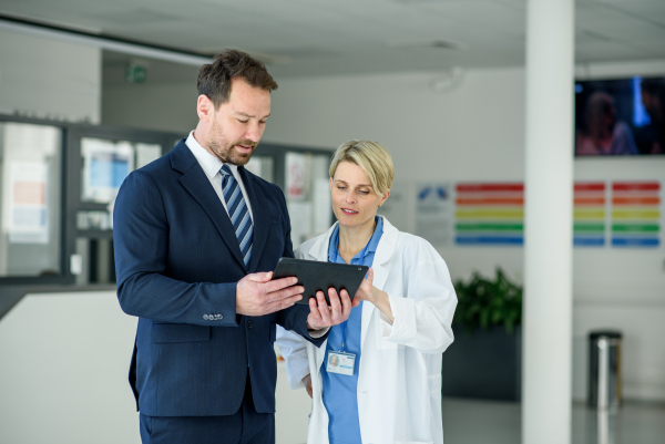 Pharmaceutical sales representative introducing new medication to female doctor, showing her presentation on tablet.