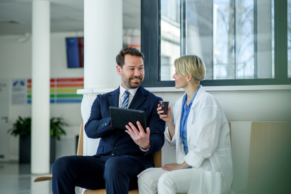 Pharmaceutical sales representative introducing new medication to female doctor, showing her presentation on tablet.