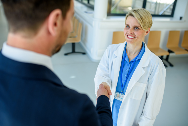 Doctor meeting pharmaceutical representative and shaking his hand in clinical setting.