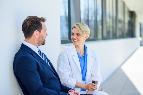 Doctor and pharmaceutical representative talking about new drug, in front of hospital building.