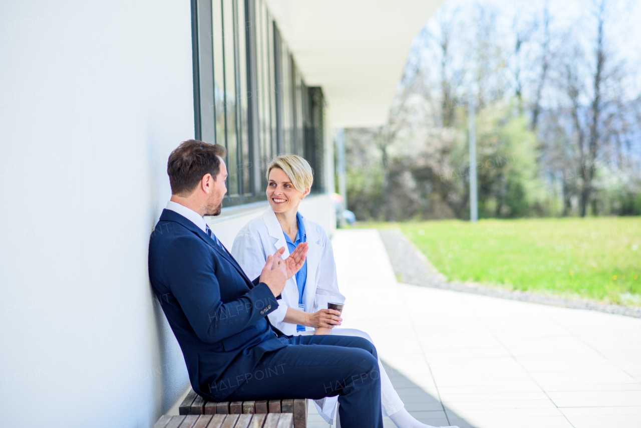 Doctor and pharmaceutical representative talking about new drug, in front of hospital building.