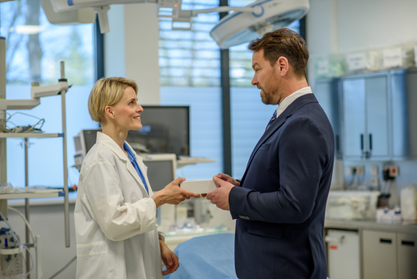 Pharmaceutical sales representative handing a sample box of new medication to female doctor in clinical setting.