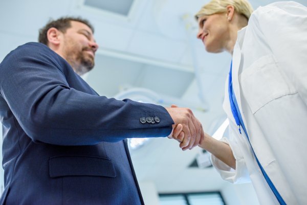 Female doctor and pharmaceutical sales representative finalizing deal and partnership in hospital setting.