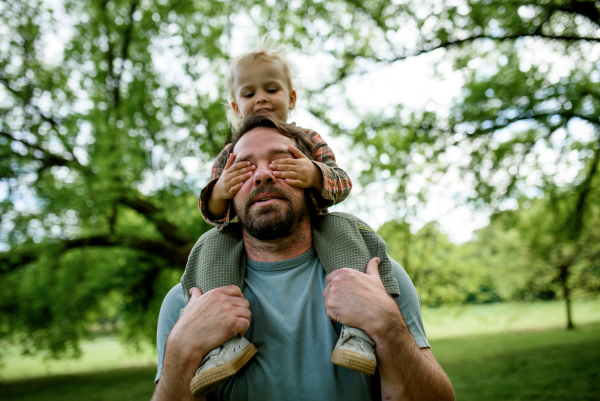 Little boy covering dad's eyes, while he carry him on shoulders Walk in park