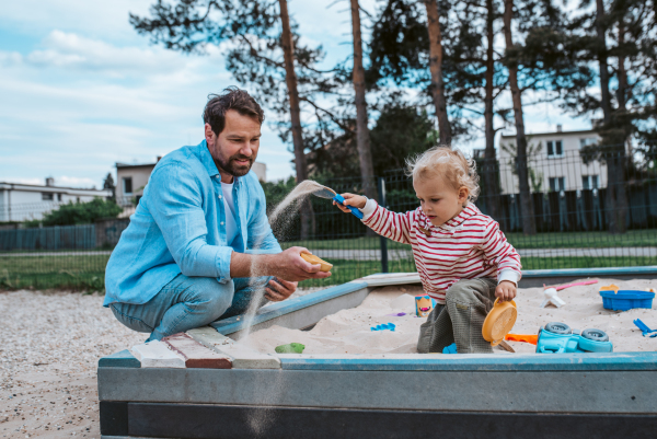 Father and little toddler son playing in the sandbox on playground, weekend fun.