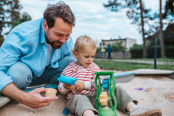 Father and little toddler son playing in the sandbox on playground, weekend fun.