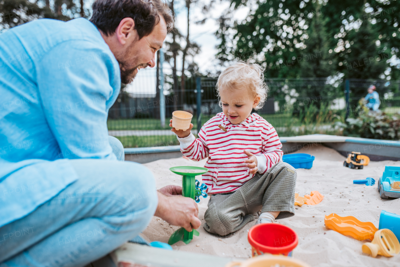 Father and little toddler son playing in the sandbox on playground, weekend fun.