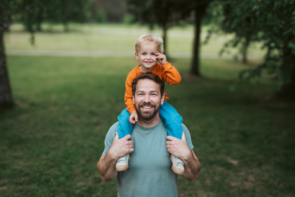 Dad carrying his smiling son on shoulders during walk in park