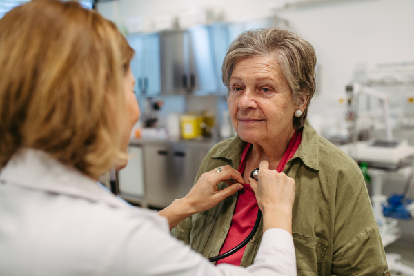 Geriatrician doctor examining elderly patient with stethoscope.. Routine health exam for elderly woman.