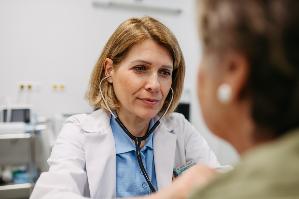 Geriatrician doctor examining elderly patient with stethoscope.. Routine health exam for elderly woman.