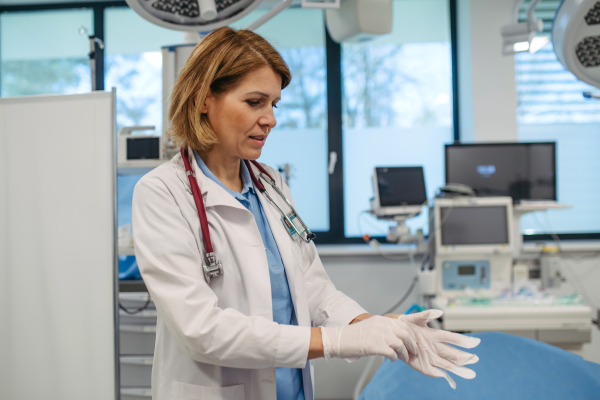 Female doctor is preparing for examination, putting on gloves. Medical setting.