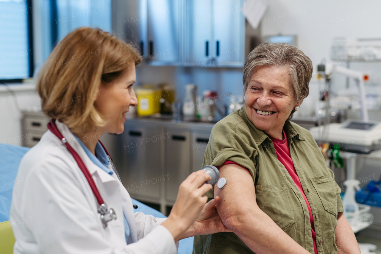 Female doctor applying CGM sensor to senior patient's arm. Medical setting.