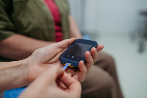 Close-up of hands using blood glucose meter during medical exam. Diabetes test.