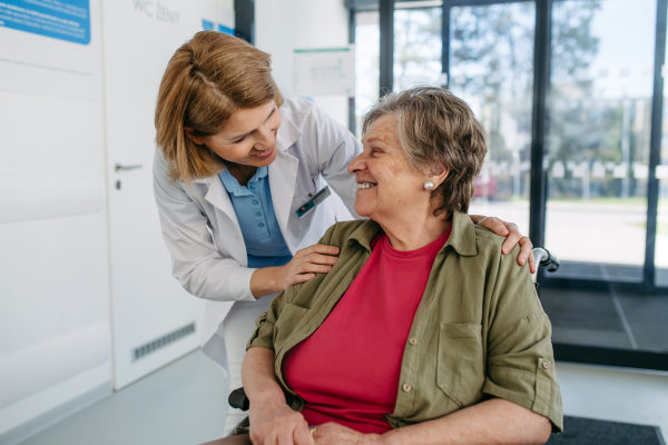 Geriatric doctor talking with patient in a wheelchair in hospital hallway. Senior health care.