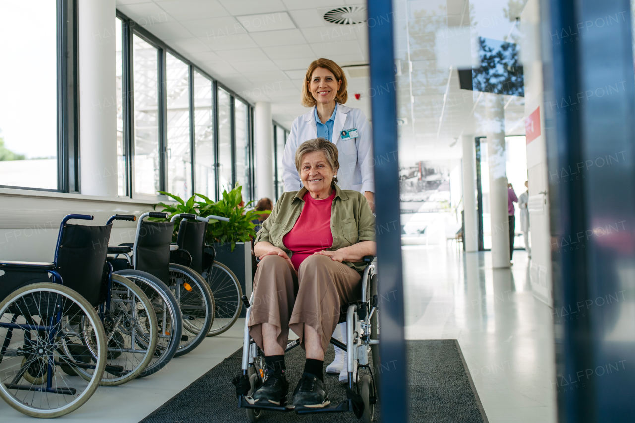 Geriatric doctor pushing a patient in a wheelchair down a hospital hallway. Senior health care.