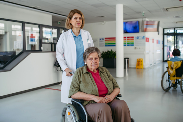 Geriatric doctor pushing a patient in a wheelchair down a hospital hallway. Senior health care.
