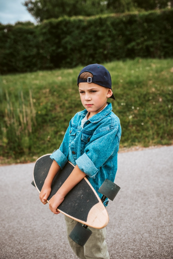 Cute boy standing on street, holding his longboard.