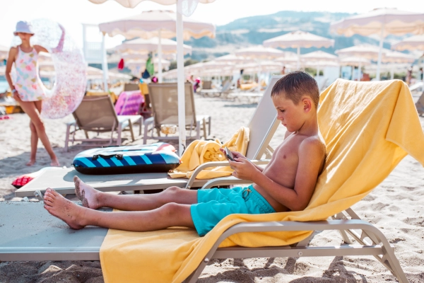 Boy relaxing on beach lounger playing game on smartphone. Summer beach holiday.