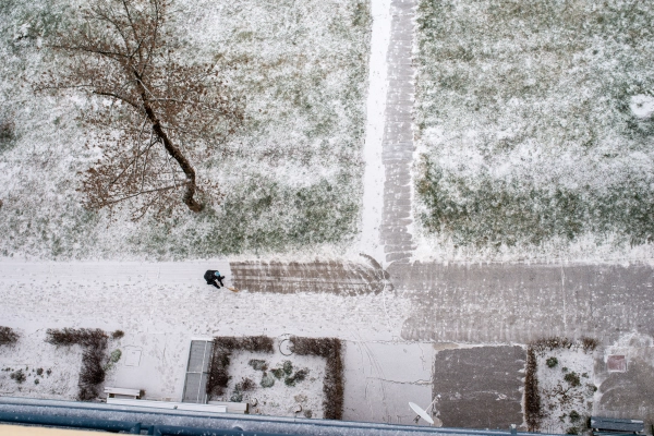 Sweeping the snowy sidewalk in front of the apartment building.